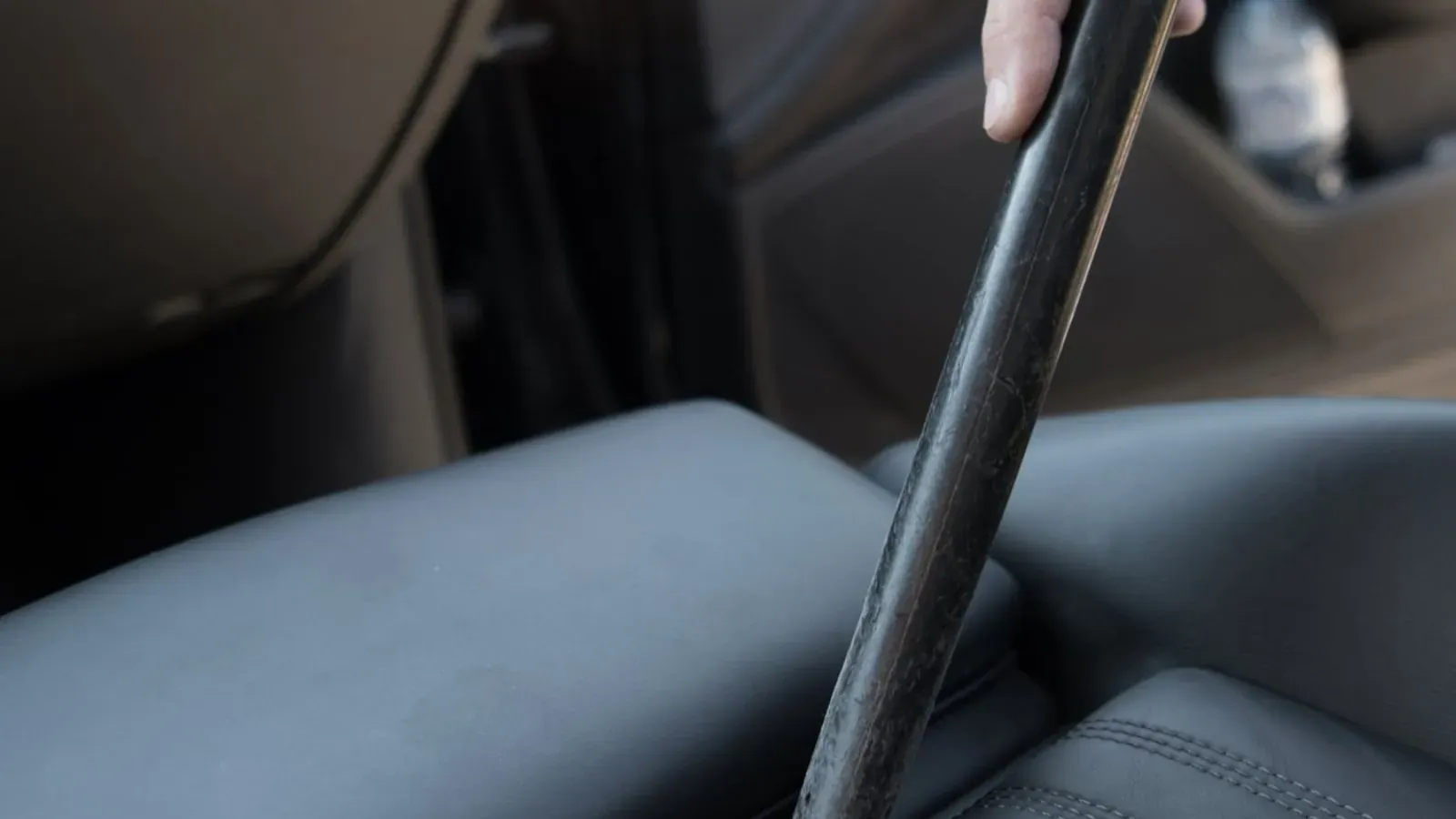 Vacuum nozzle cleaning the gap between a black leather seat and the centre console