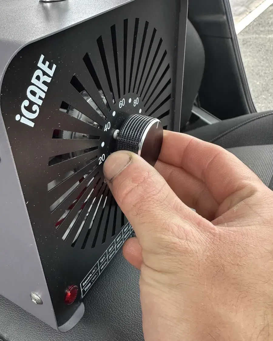 Hand setting the timer on an ozone generator placed inside a car